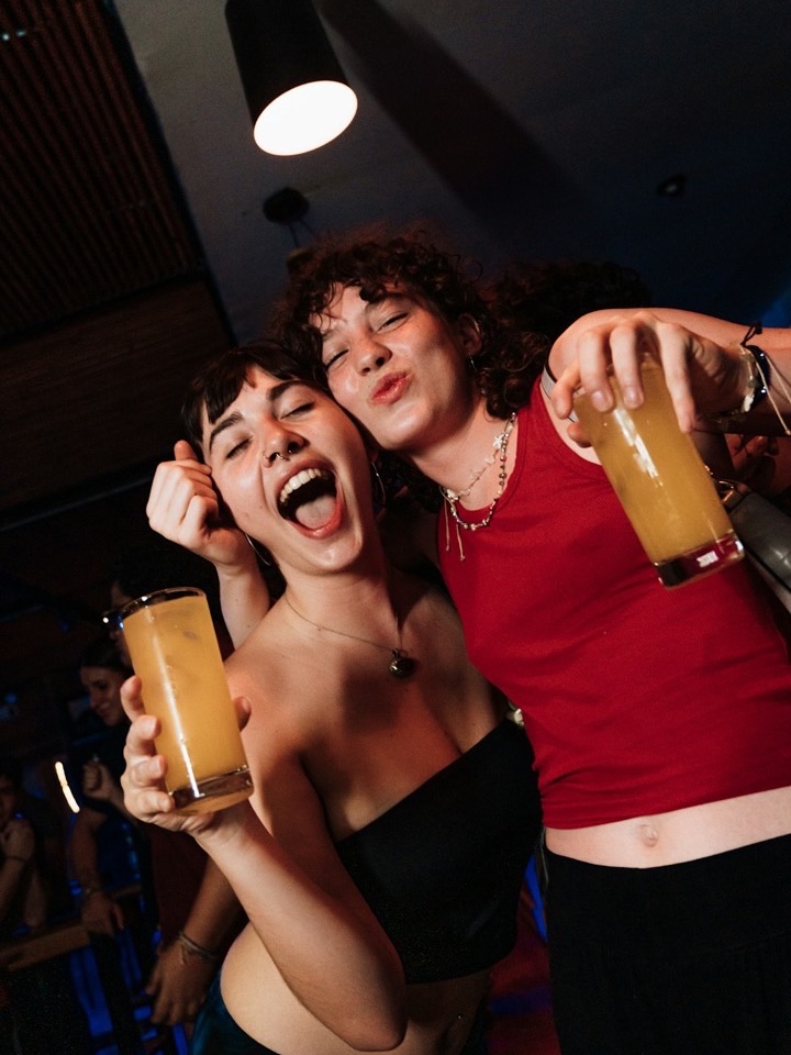 Two friends laughing with drinks under the flash, posted by maya